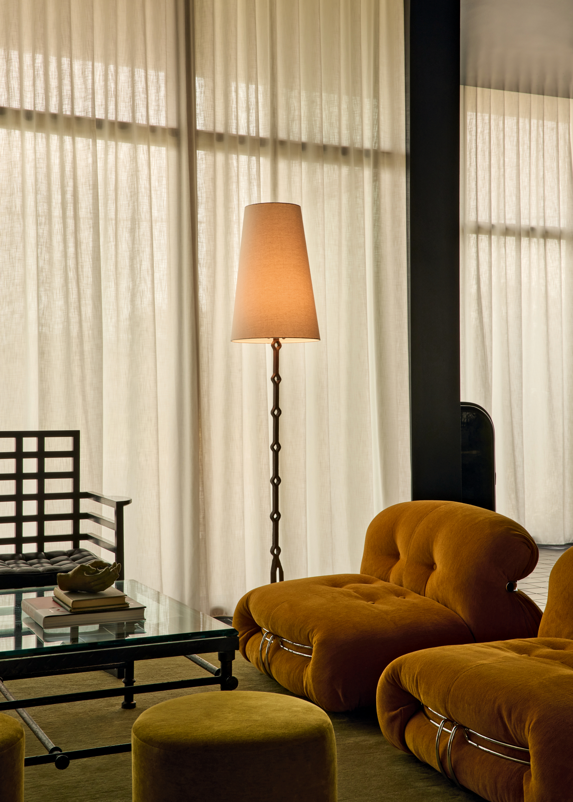 Corner of a living room with mustard low-slung armchairs, grey velvet footstool and rug, and black accent chair
