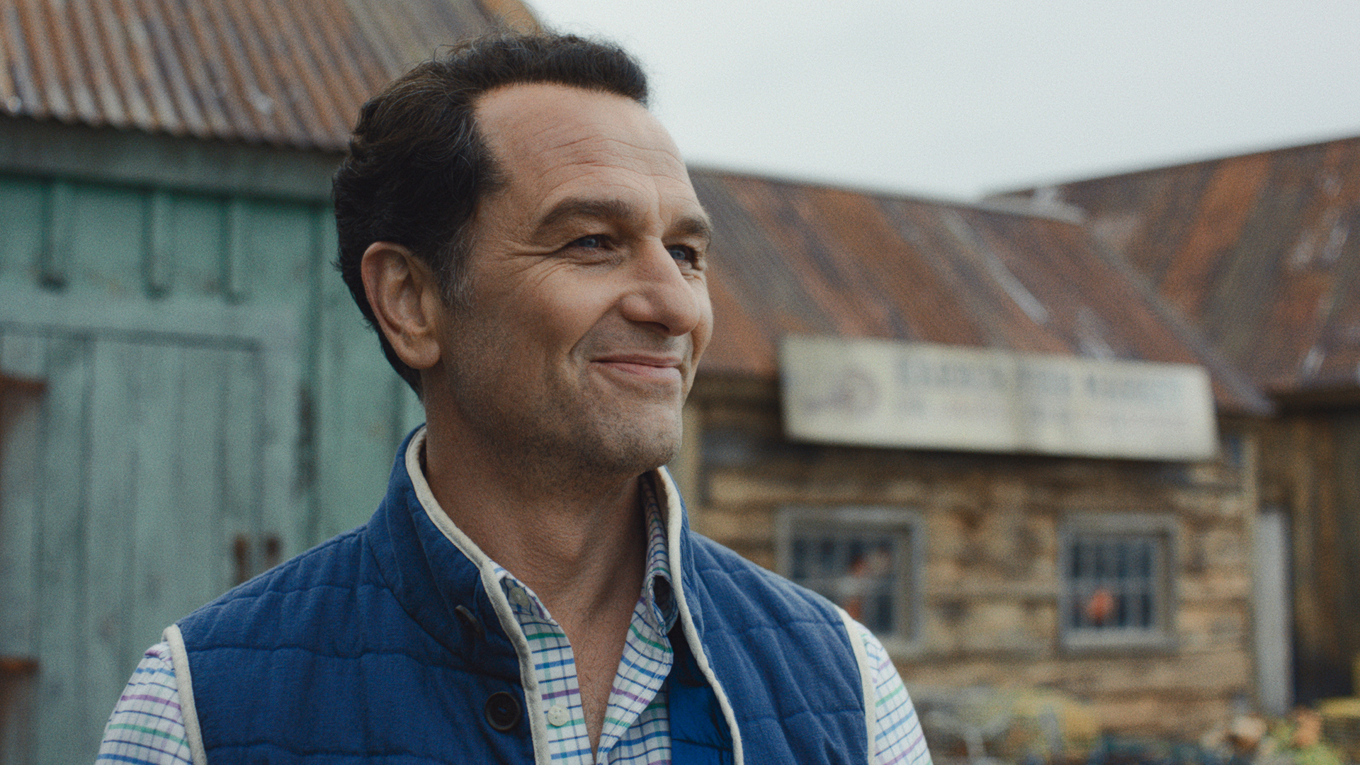 Matthew Rhys' Tom Loftis smiling as he stands outside in Widow's Bay