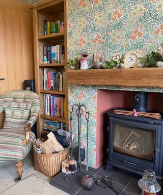 A living room with floral wallpaper, a wooden bookcase, a fireplace, and a multicolored chair