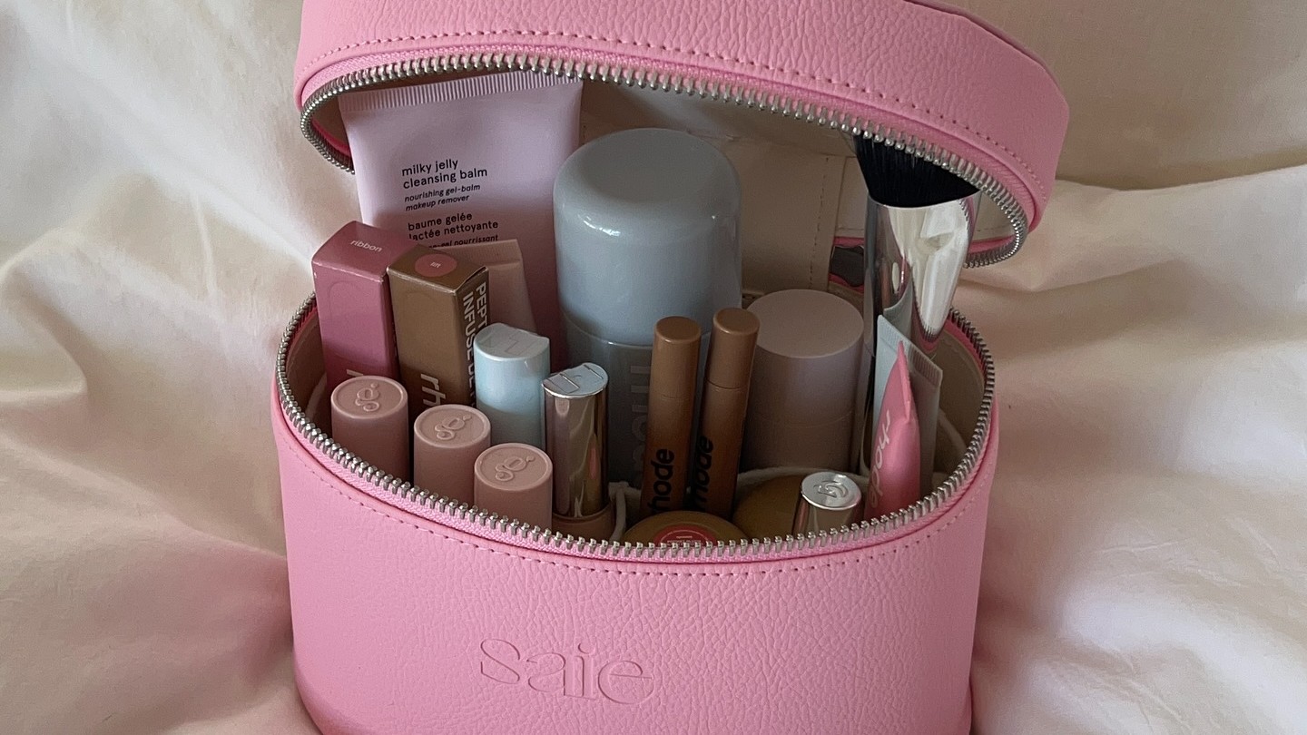 Photo of a full, pink makeup bag resting on a bed 