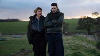 Moira talking to a sad looking Ross, who has his arms folded, and both are standing in a field