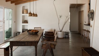 discovering your interior design style, rustic dining room with large table and wood and rattan chairs, concrete floor, beams, brass pendant lights, alcove storage, plants 