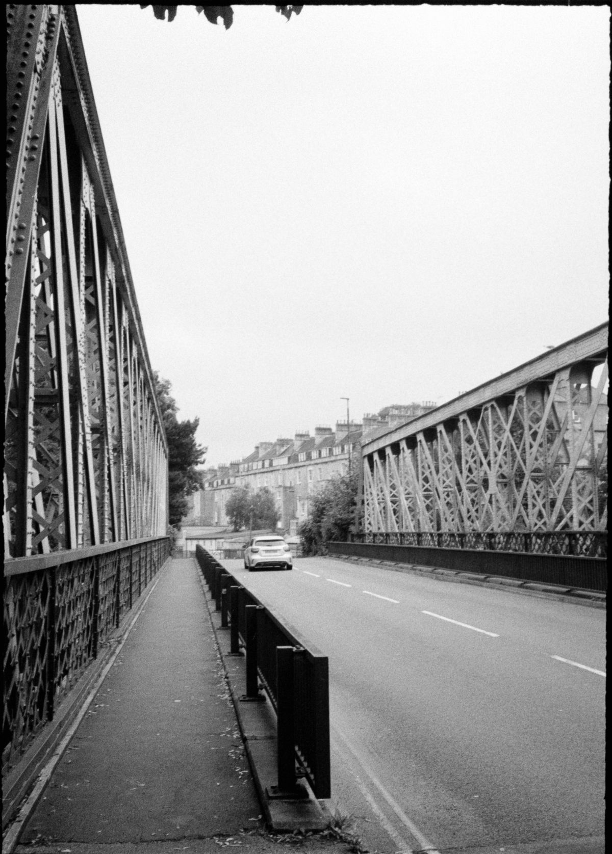 A road crossing a large iron bridge with a car driving across it