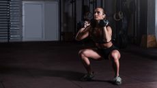 A woman performing front rack squat with dumbbells