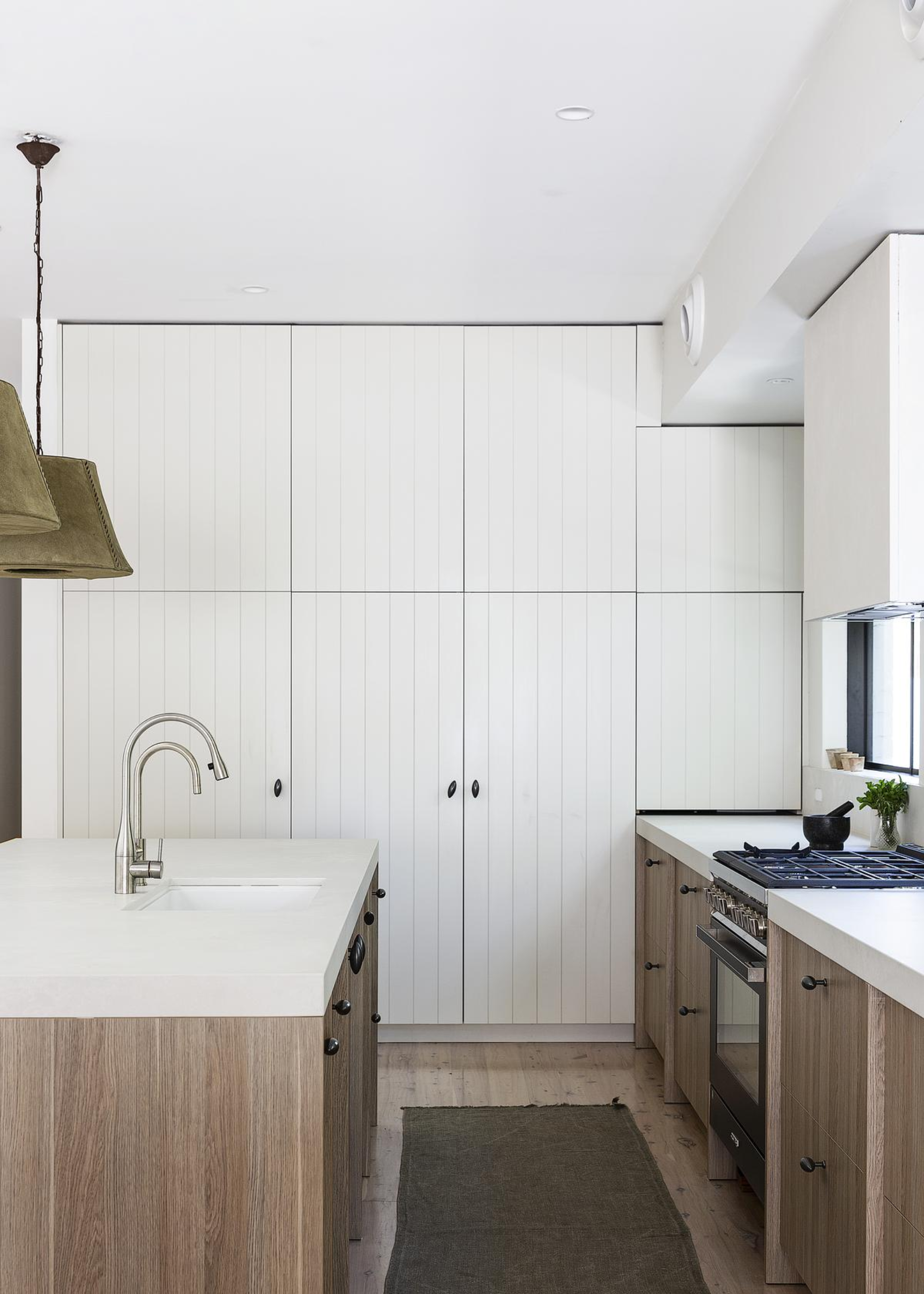 A kitchen with an island as well as counter space both holding quartz worktops. On the island is a sink and tap and on the other counter is a gas stove top