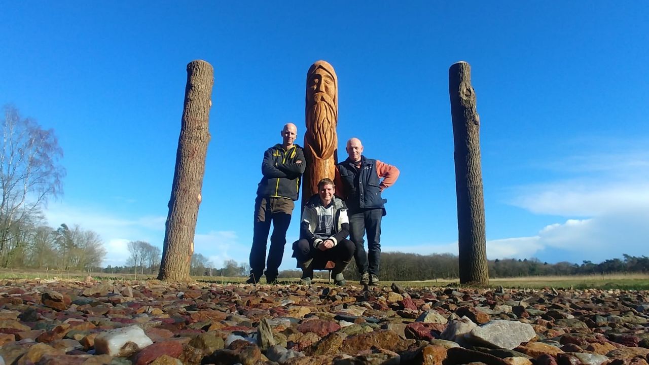 A photo of three men standing around a reconstructed pagan post with a human figure