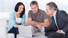A couple talk with an adviser while sitting on their sofa and looking at a laptop.