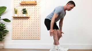 man performing a standing hamstring stretch in a studio setting