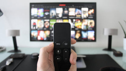 The best TV's in the UK: blurred out image of widescrren TV with Netflix on, hand holding remote in forefront