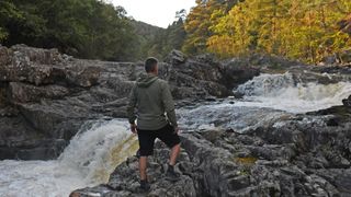 Hiker next to stream wearing a Montane Khamsin Hooded Softshell Jacket