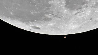 A telescope photo of the Red Planet Mars rising near the bottom of Earth's moon