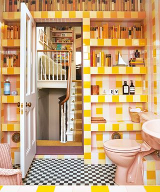 Colorful, pink and yellow tiled bathroom, niche shelving displaying ornaments and decorative ornaments, pink toilet, checkered flooring