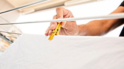 Someone hanging white sheet on an airer with a yellow clothes peg