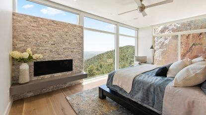 Bright bedroom with wall to ceiling windows and stone accents, including on a wall behind a fireplace with floating mantel, and on the wall to the right as art