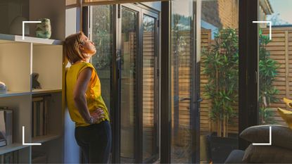 Woman looking out of window into the sunset from living room and relaxing, representing how to stop worrying