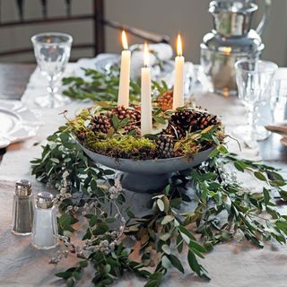 table with raised bowl filled with moss, pine cones and candles