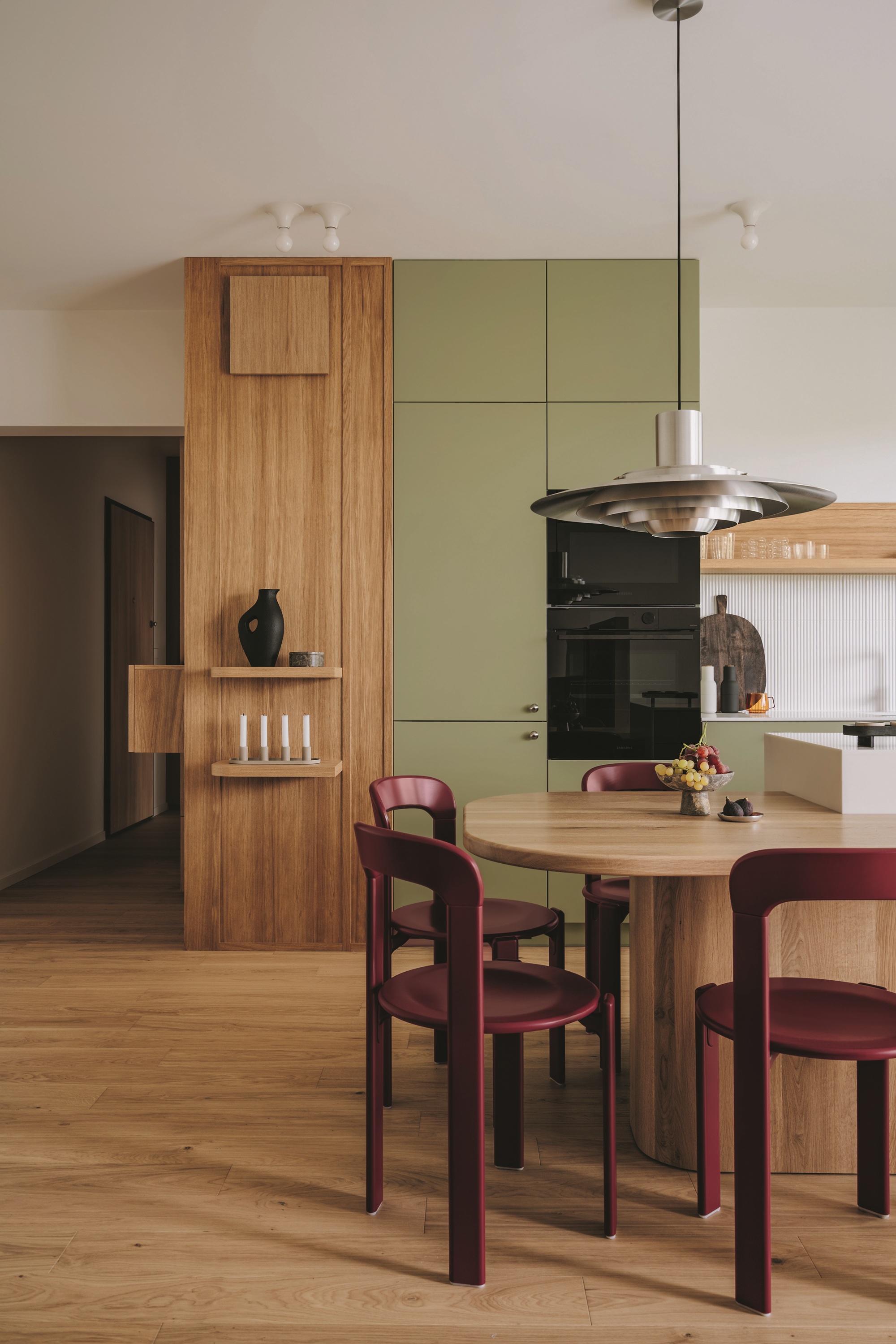 matcha green and timber kitchen with burgundy chairs around a timber island bench with a chrome pendant light hanging over and white fluted backsplash