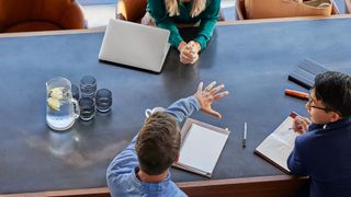 An overhead photo of three business people sitting at a board table and brainstorming