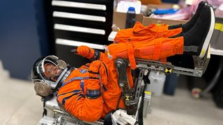 an astronaut giving a thumbs-up inside a spacesuit, while lying on his back near a filing cabinet