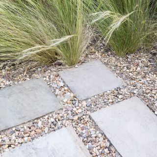Stepping stones on gravel path surrounded by long grasses