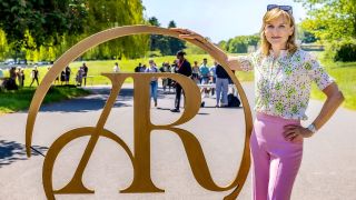 Host Fiona Bruce stands alongside a metal Antiques Roadshow logo