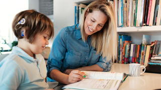 A woman and young girl sitting at a desk and learning from an exercise book