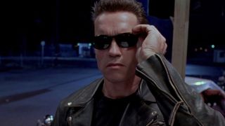 Still from Terminator movie. A cyborg who looks like a human man with short dark hair is wearing a black leather jacket and has just put on some black sunglasses.