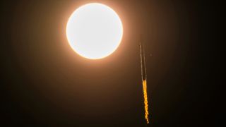 a rocket is seen in slihouette launching to space as it appears to pass by the sun