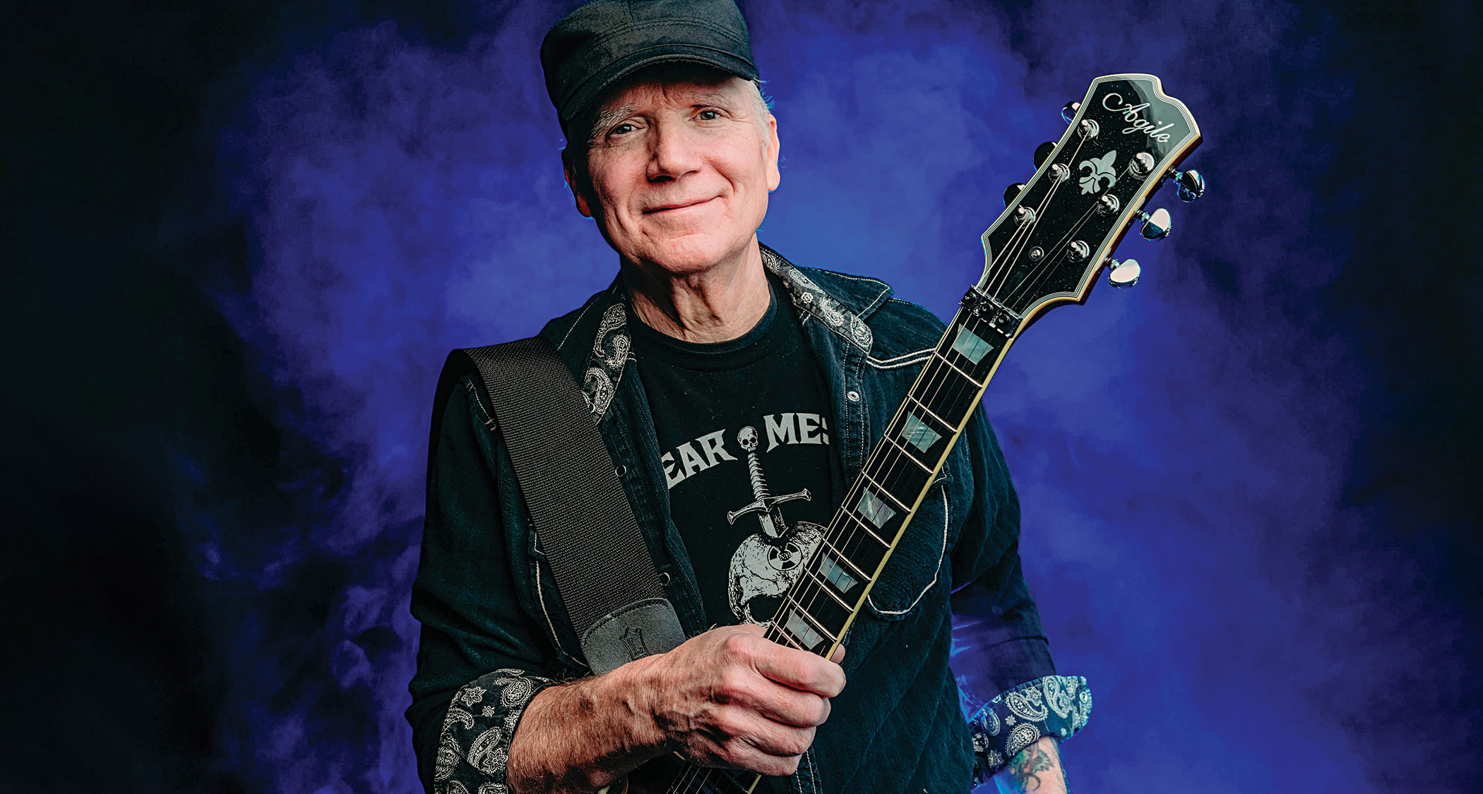 Chris Poland with an Agile electric guitar, pictured in front of blue smoke-effect background.