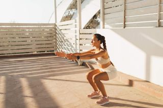 A woman doing squats on her balcony at home.