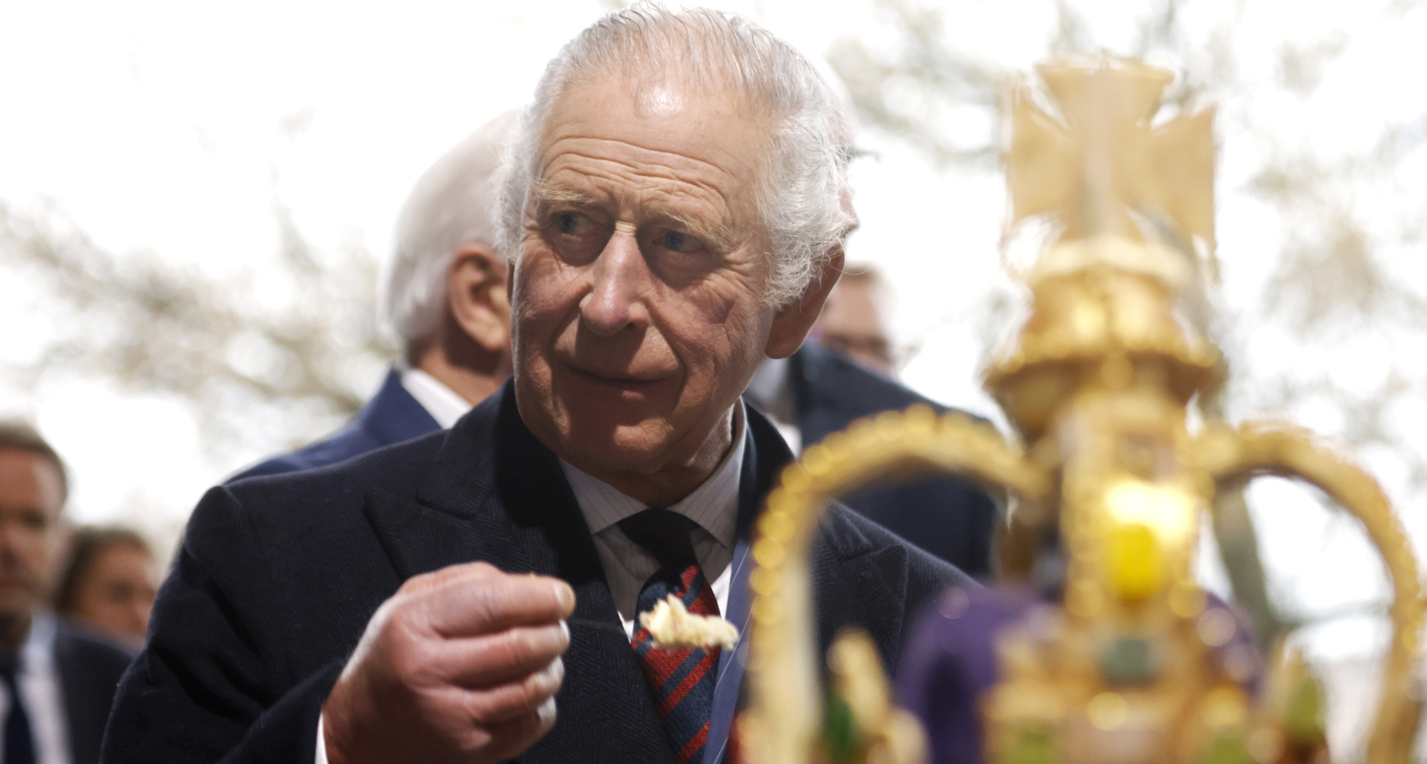 King Charles holding a spoonful of food in front of a crown cake