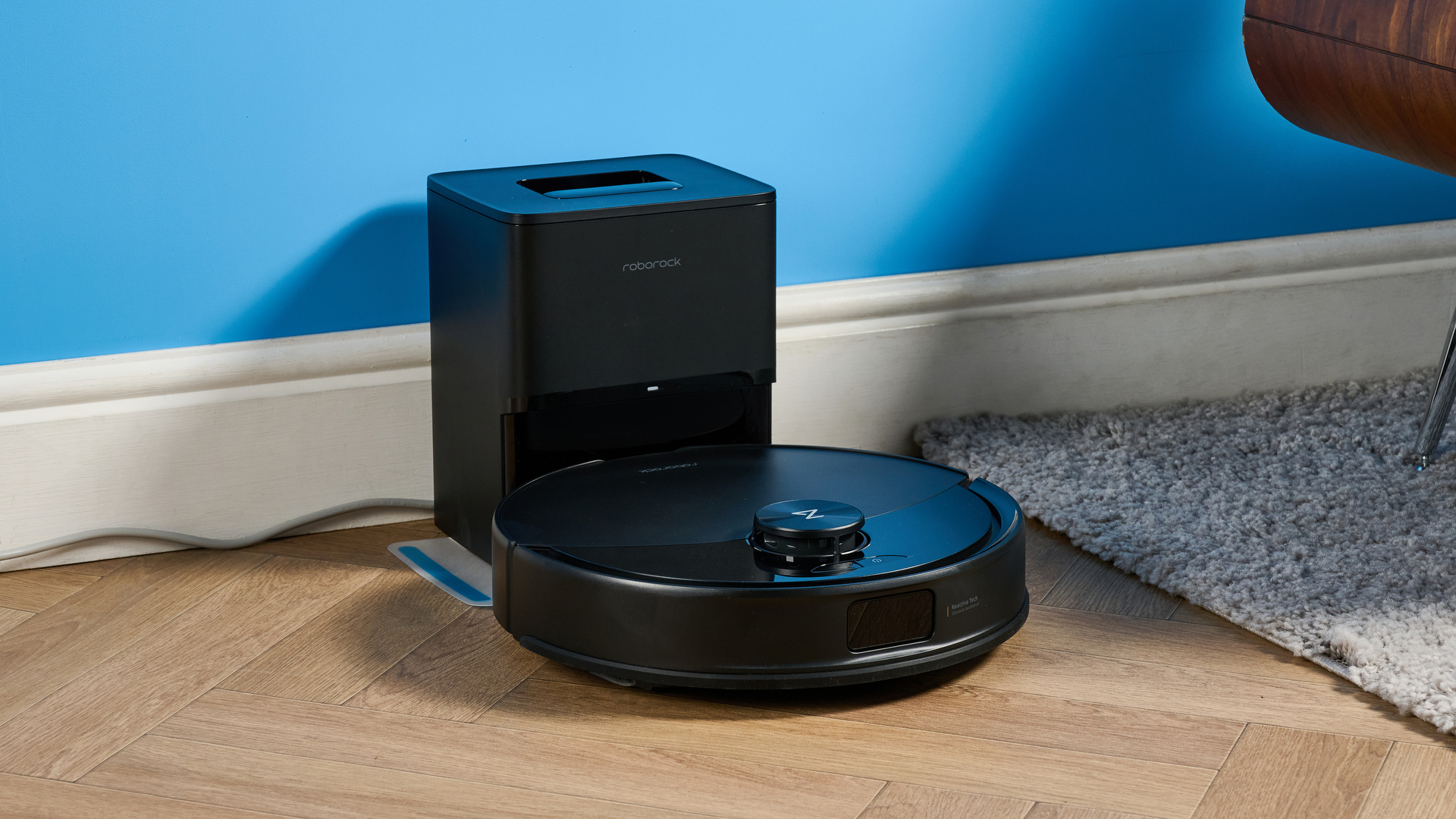 Roborock Q10 S5+ photographed on a wooden floor in front of a blue background
