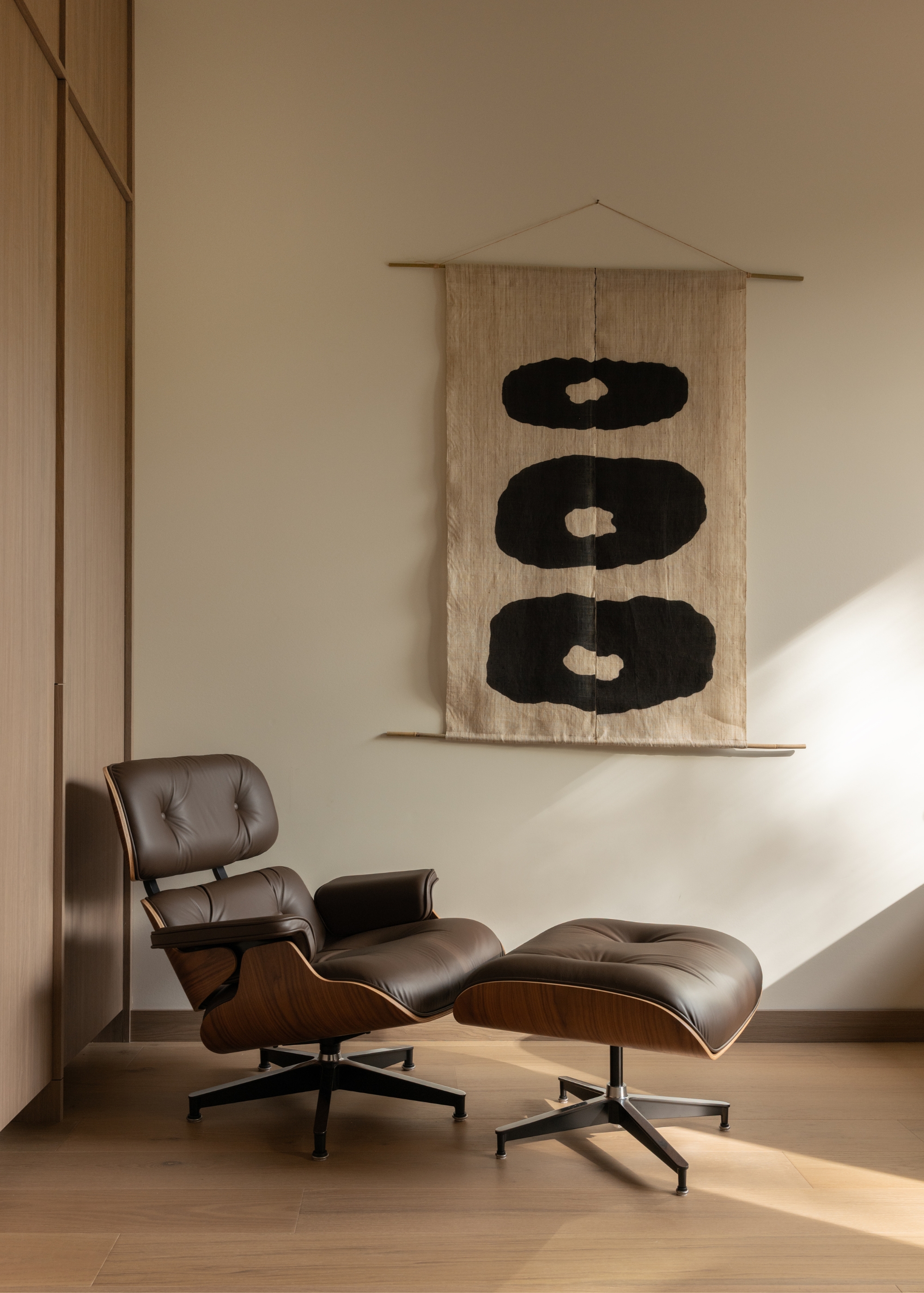 A brown leather Eames chair in a living room beside a black and white wall hanging