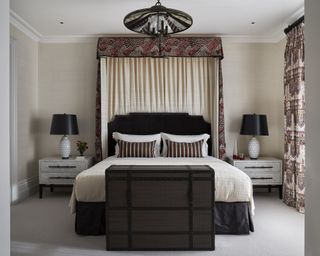 A sand colored bedroom with a black headboard and lamps, and a canopy with red patterned fabric