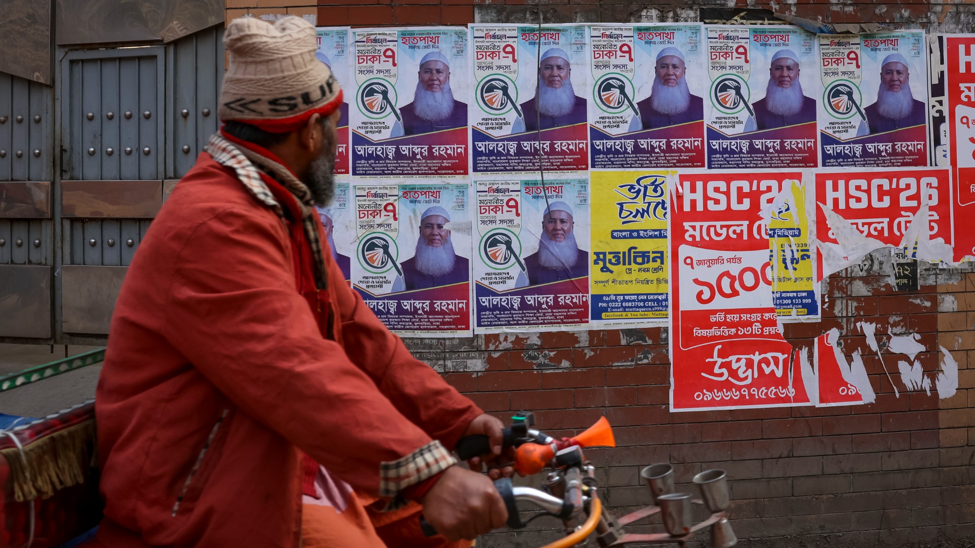 A man on a bicycle looks at election posters pasted on a wall in Dhaka, Bangladesh