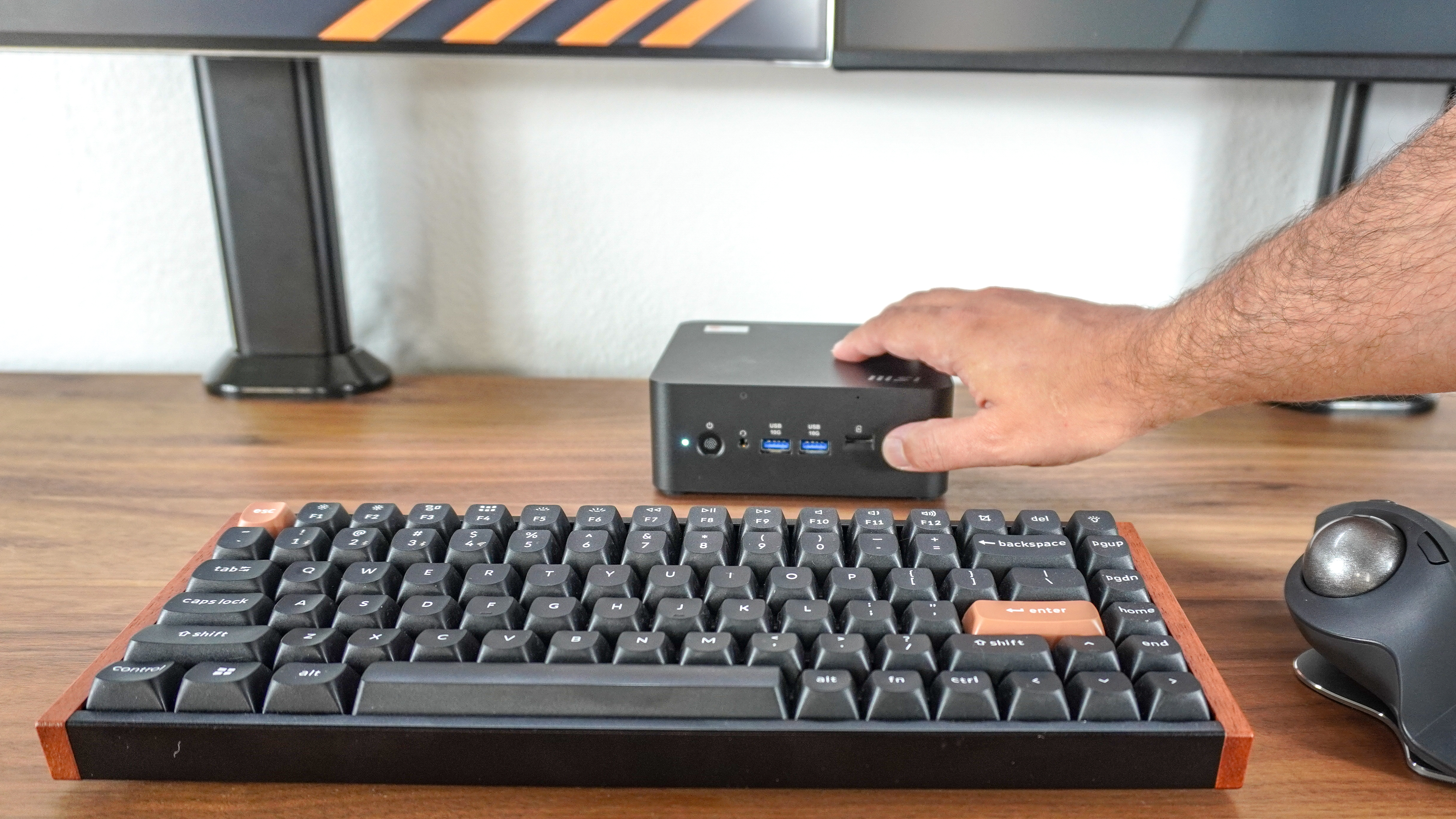 A person reaching across their desk to press the dedicated Copilot button on the front of the MSI Cubi NUC AI+ 2MG mini PC