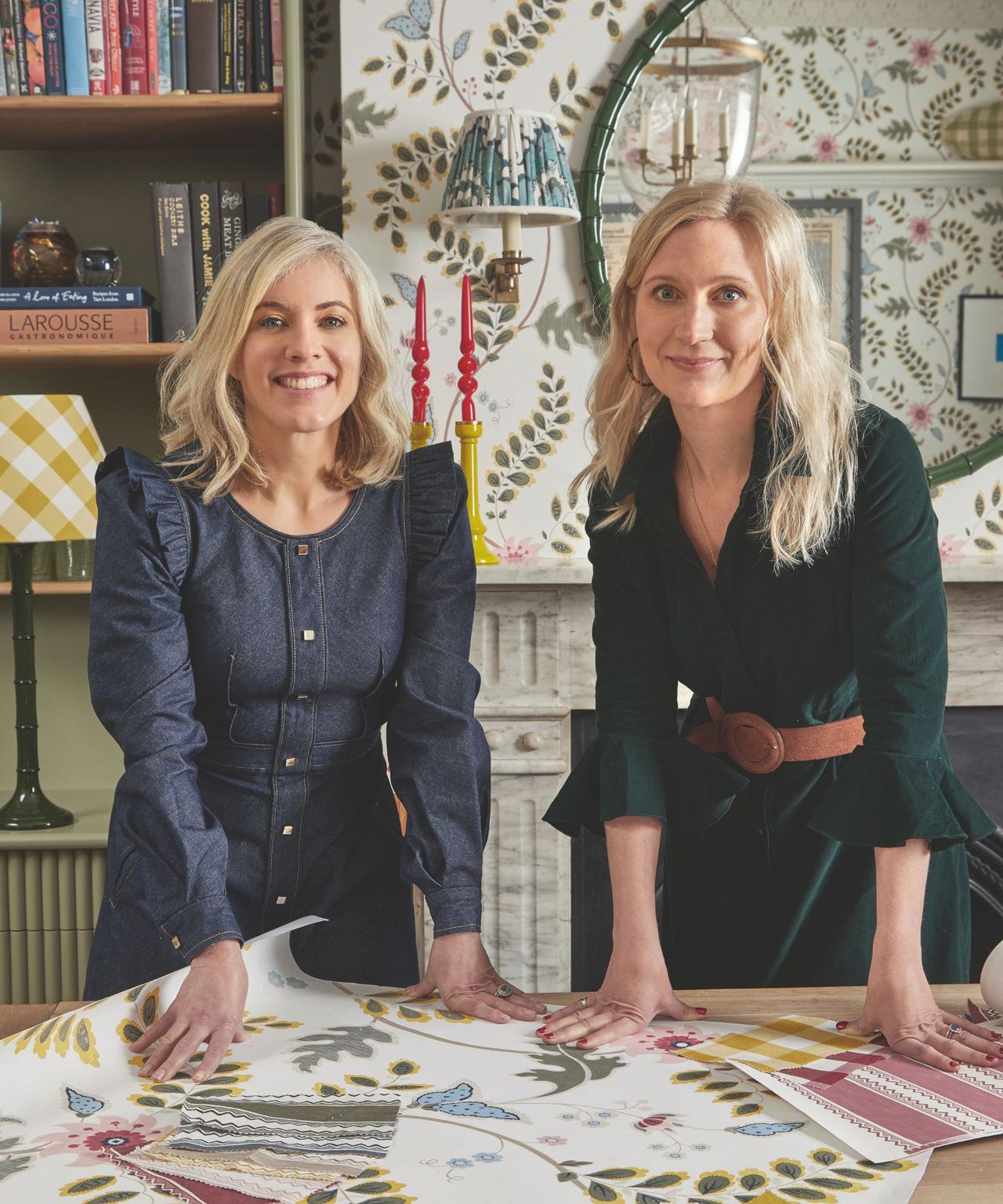 Two women stand leaning at a table with scattered wallpaper samples