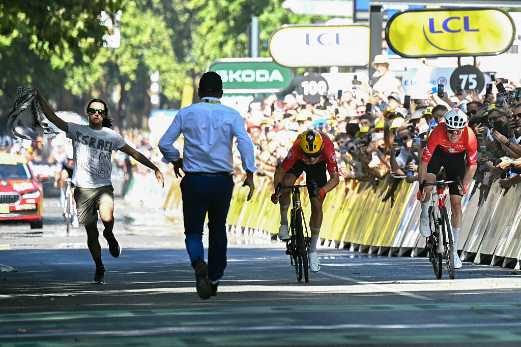 A Tour de France staff member attempts to intercept an individual running at the finish line area as Uno-X Mobility team's Norwegian rider Jonas Abrahamsen (C) cycles ahead of Team Jayco AlUla team's Swiss rider Mauro Schmid (R) to the finish line to win the 11th stage of the 112th edition of the Tour de France cycling race, 156.8 km starting and finishing in Toulouse, southwestern France, on July 16, 2025. (Photo by Loic VENANCE / AFP)