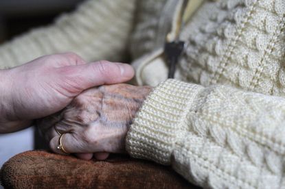 A woman holds her elderly relative's hand.