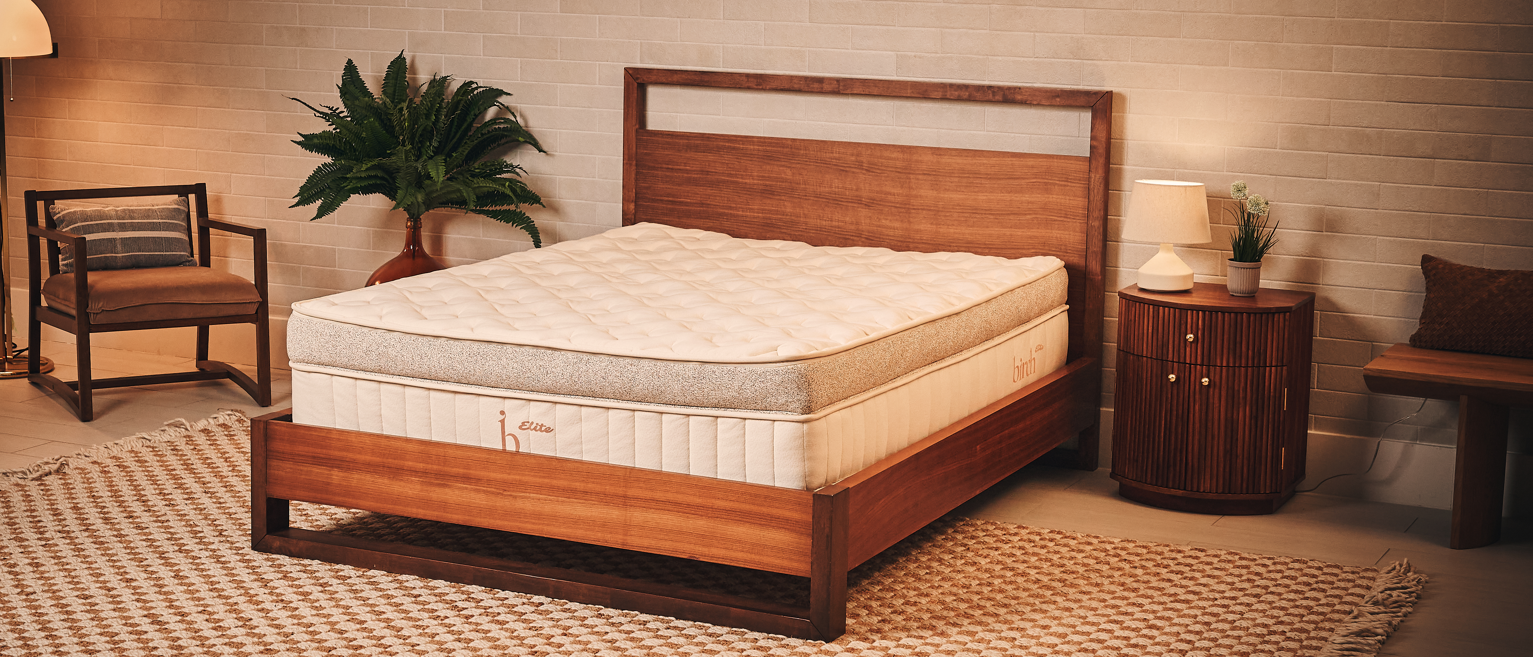 The image shows a beige and brown mattress placed on a wooden bed frame in a neutrally decorated bedroom