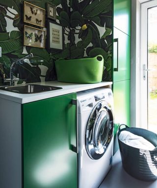 A laundry room with green palm print wallpaper wall decor and washing machine with green rubber basket