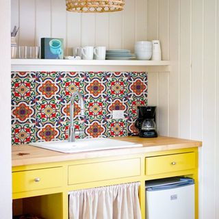 Colorful patterned tiles on kitchen backsplash, with yellow painted cabinets, and wall paneling.