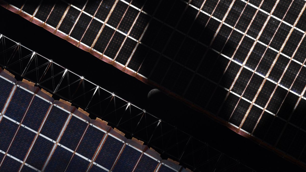 The eclipsed moon peeking through the solar panels of the International Space Station