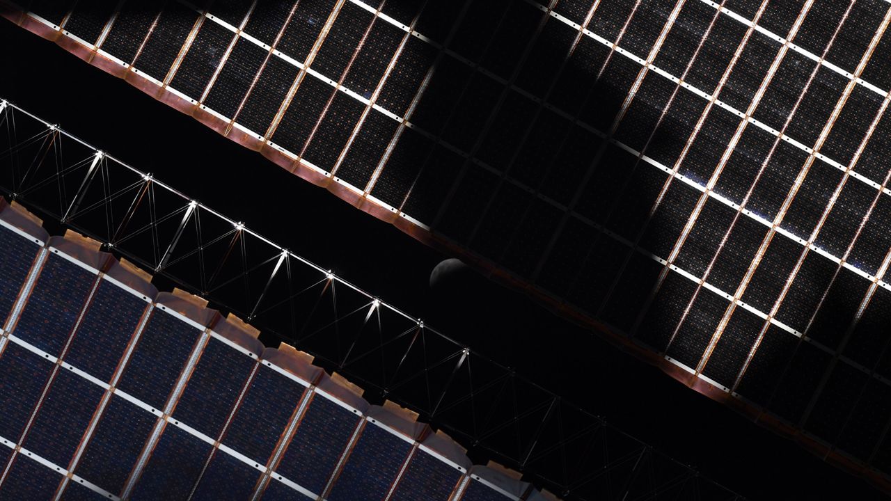The eclipsed moon peeking through the solar panels of the International Space Station