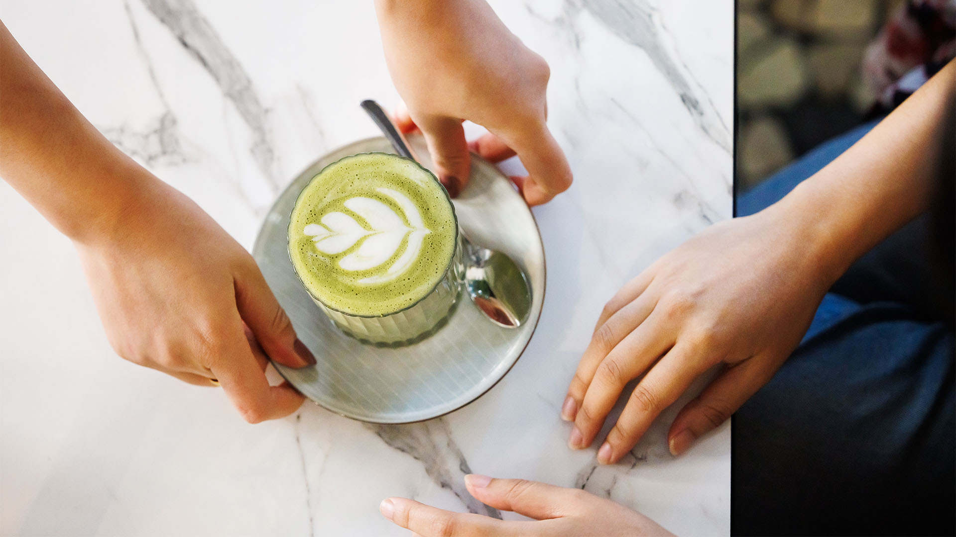 A close up of a pair of hands passing a cup filled with a matcha latter to another person
