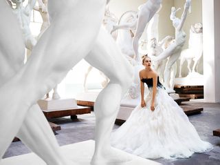 Woman in a black and white ballgown, surrounded by white statues in various poses