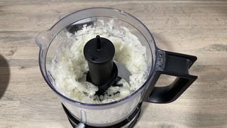 A close up view of chopped onion pieces inside the KitchenAid Mini Food Chopper work bowl.