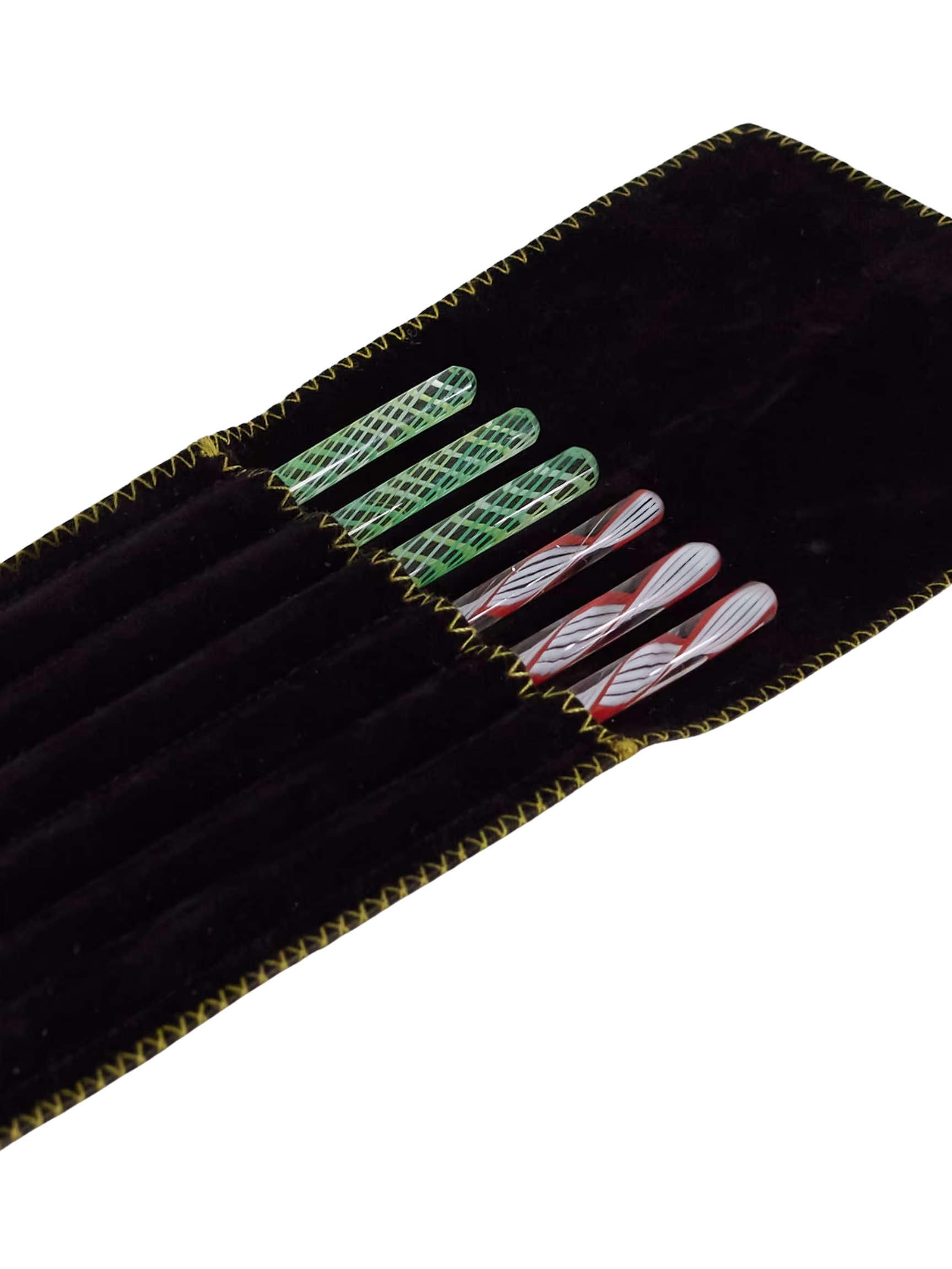 A velvety, leather black folder stores six cocktail sticks in colorful Murano glass, three in green and transparent glass, three in red, white, and black glass.