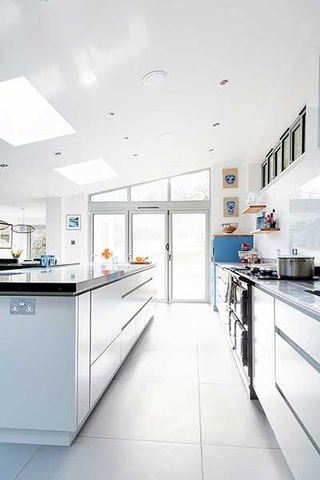 a modern, all-white kitchen extension, with white units, white tiled floor, black countertops, and doors to the garden
