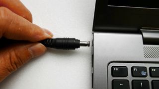 a hand plugging in an AC adaptor into a laptop